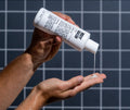 Person holding a bottle of Kiehl's body wash and pouring it into their hand against a grid background.