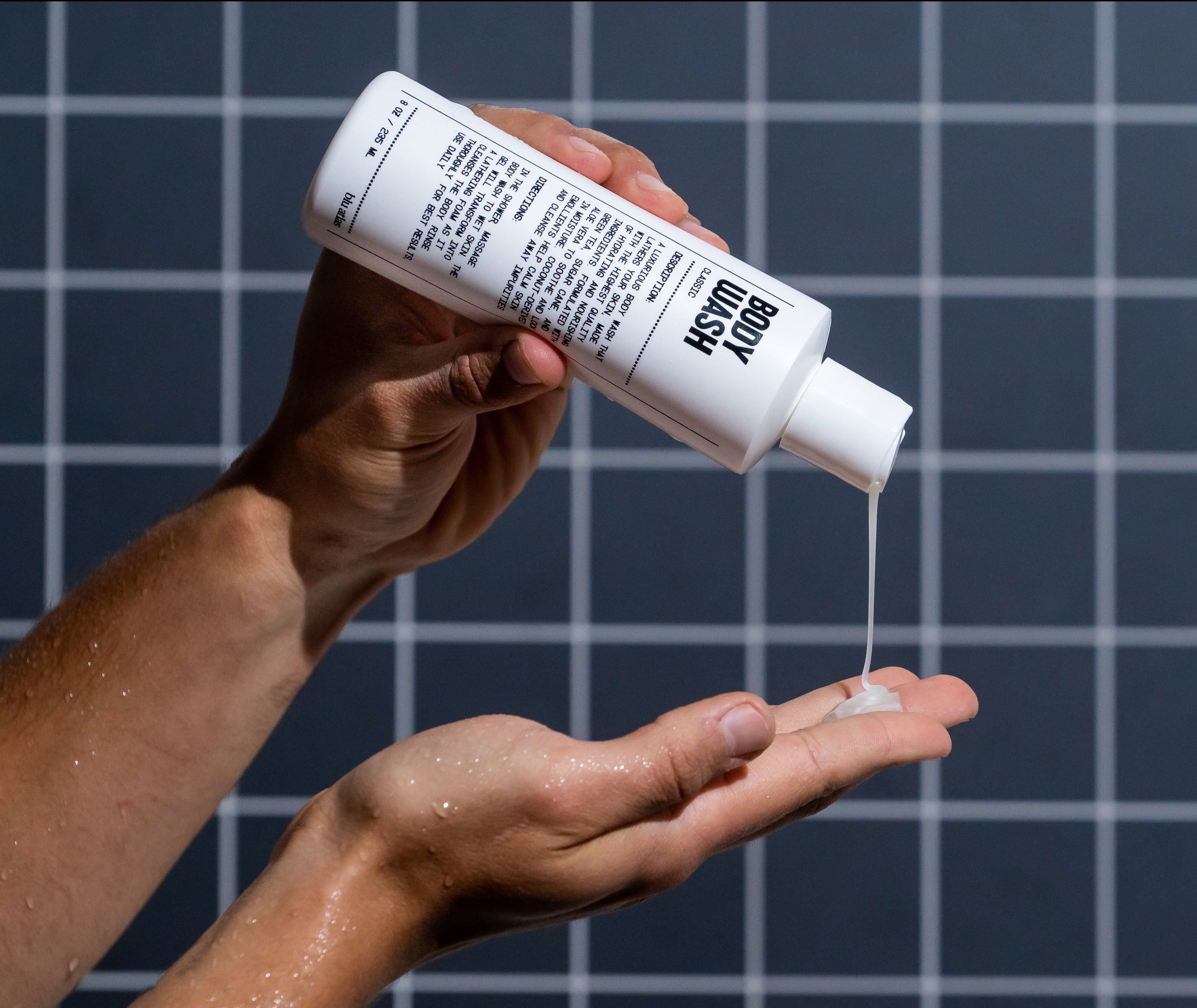 Person holding a bottle of Kiehl's body wash and pouring it into their hand against a grid background.