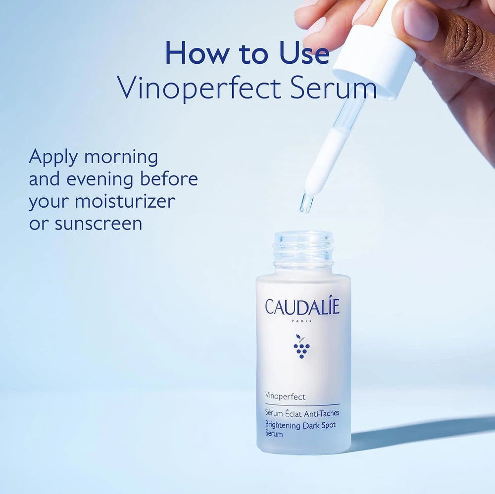 A hand holds a white dropper above an open bottle of Caudalie Vinoperfect Serum against a soft light blue background, with text explaining how to use the serum.