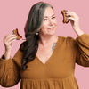 Woman holding two small brown shoes against a pink background