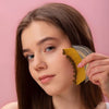 Woman using a brush on her face against a pink background