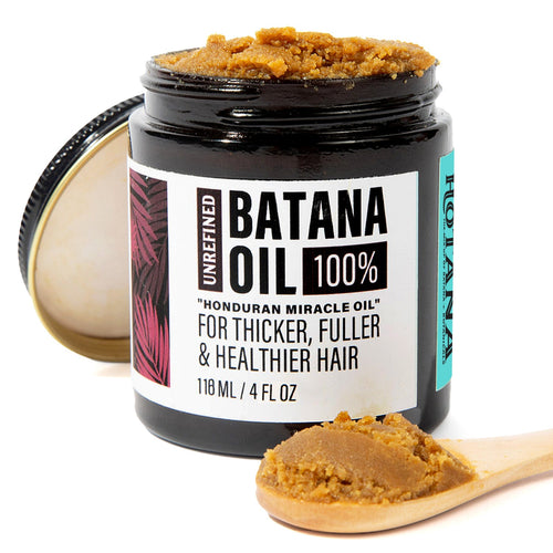 A jar of Unrefined Banana Oil hair treatment with its lid off, showing the thick brown paste inside. A small wooden spoon in the foreground holds more of the brown oil, set against a clean white background.