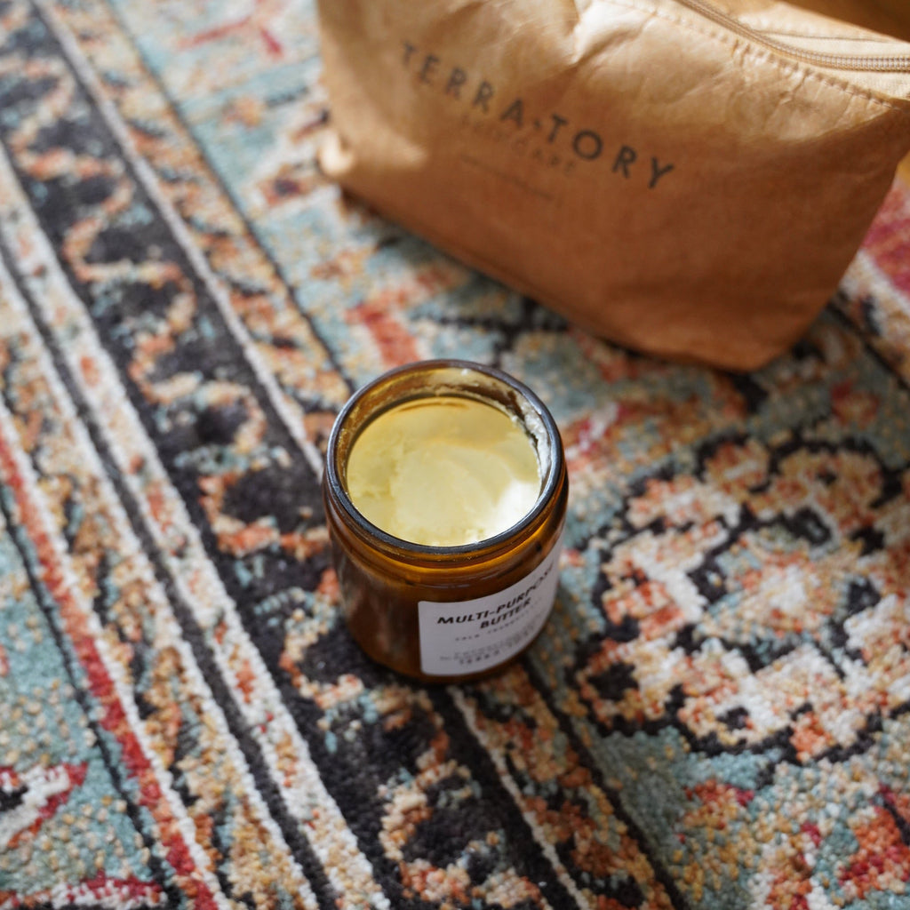 Jar of cream on a patterned rug with 'Terra Tory' bag in the background
