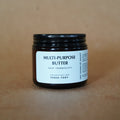 Black jar of multi-purpose butter with a white label on a brown background