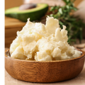 Mashed potatoes in a wooden bowl with an avocado in the background