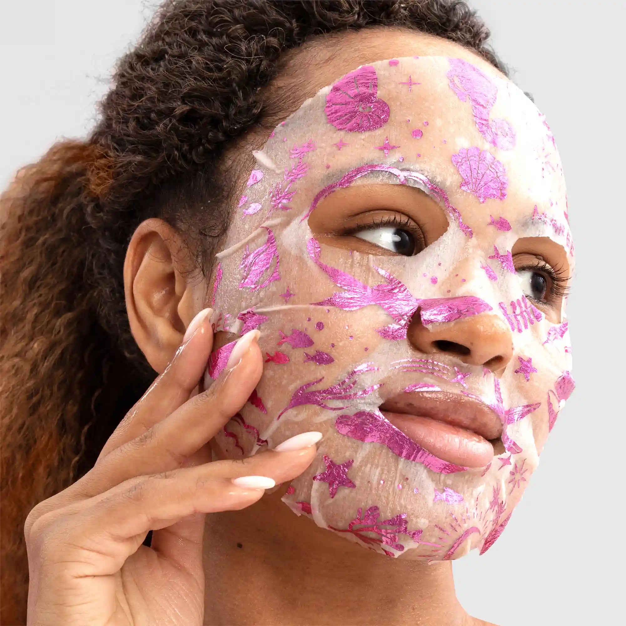 Woman applying a pink floral face mask on a gray background