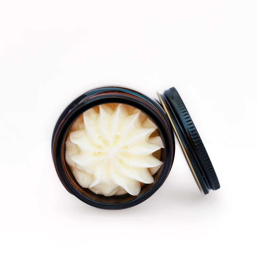 Open jar of white cream with a black lid on a white background
