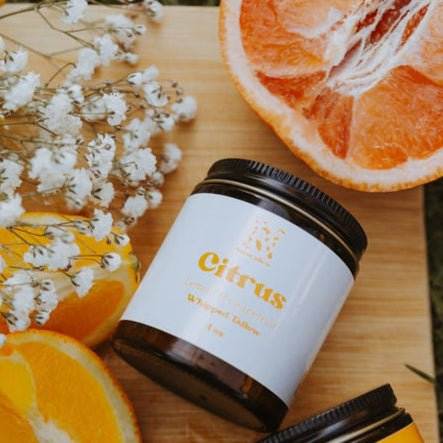 Jar of 'Citrus' body scrub with sliced oranges and flowers on a wooden surface
