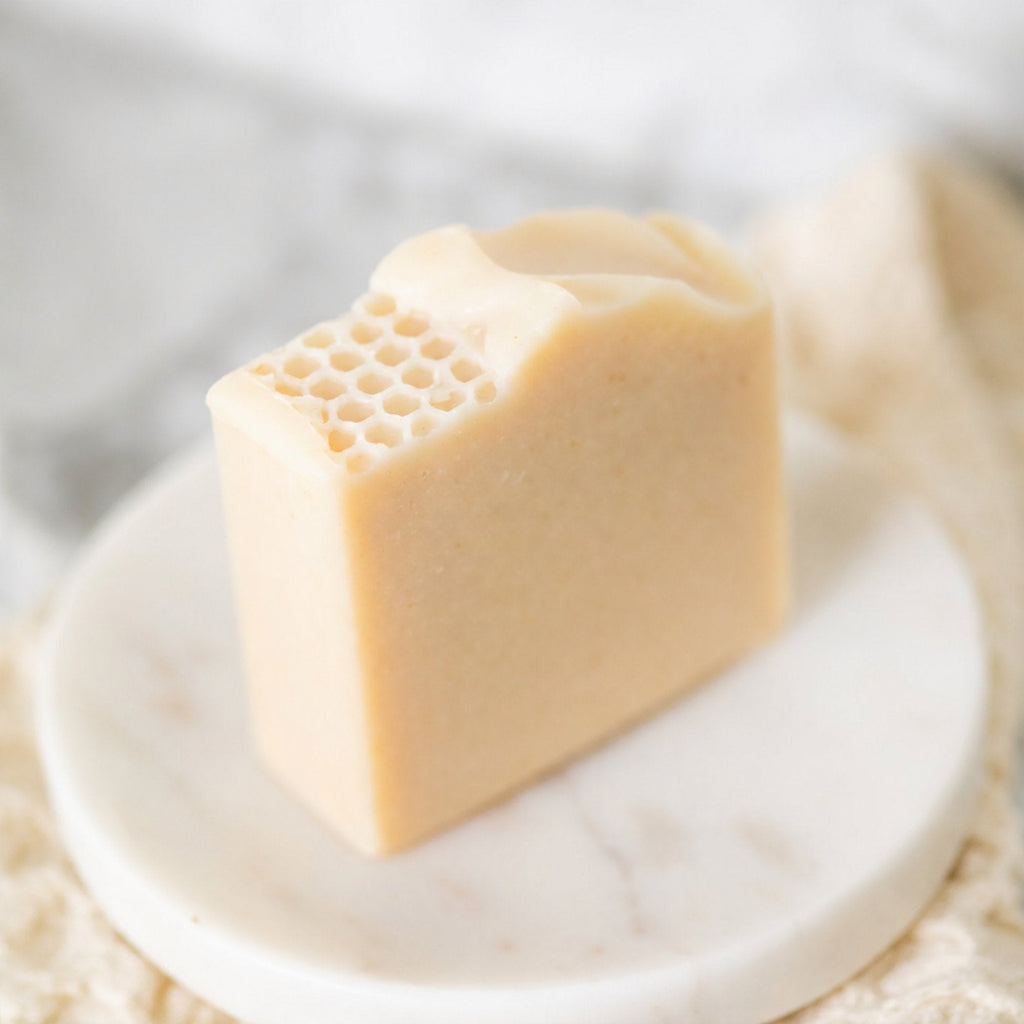 A rectangular bar of pale beige handmade soap with a honeycomb pattern on one end, displayed on a small round white marble dish.