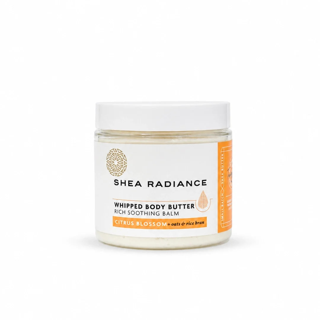 A jar of Shea Radiance Whipped Body Butter on a clean white background. The jar is clear glass showing a creamy off-white balm inside, with a white lid and a white label featuring black text and orange accents.