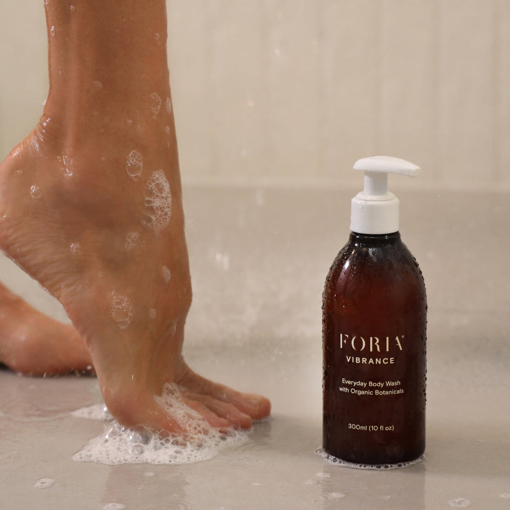 Person washing feet with FORIA body wash in a shower setting