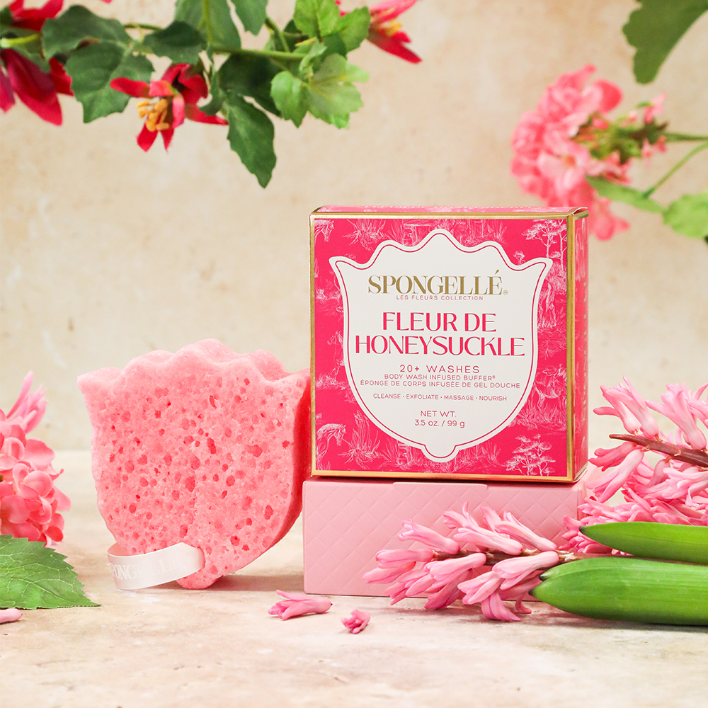 Spongelle Fleur de Honeysuckle soap bar with packaging and pink flowers on a wooden surface.