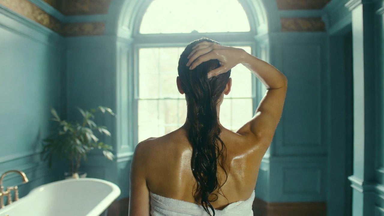 Woman in a towel standing in a bathroom with blue walls and a large window.