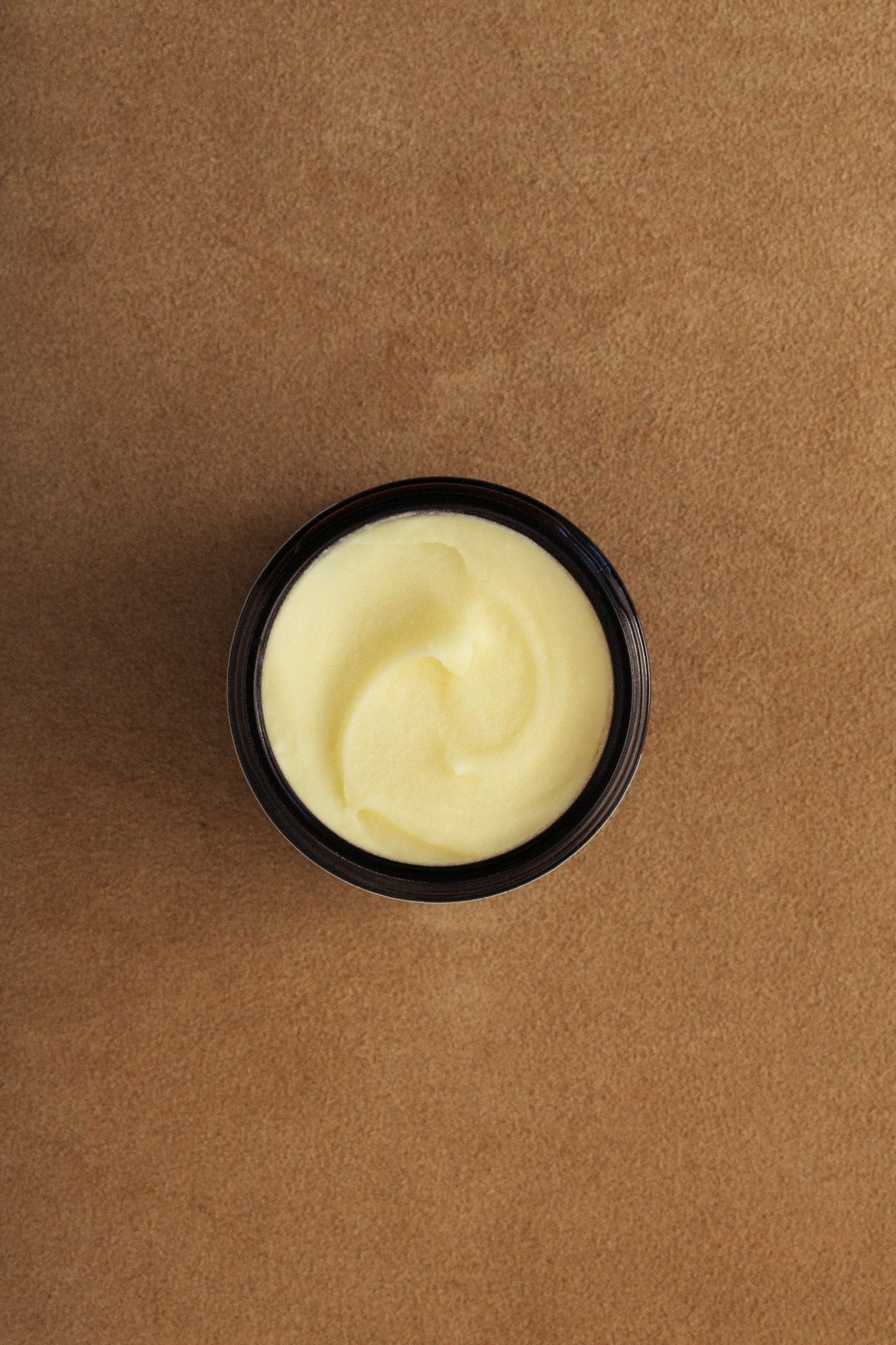 Black container with yellowish cream on a brown background